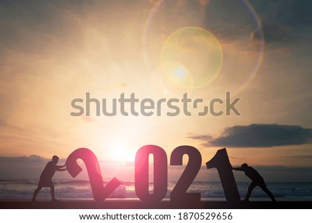 Welcome merry Christmas and happy new year in 2021,Silhouette Men pushing 2021 number on the beach with sunlight and sky.