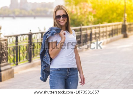 Portrait of a happy and attractive blonde Caucasian young woman in a casual denim jacket outdoors in a park on a sunny autumn day. A concept of lifestyle, happiness and joy.