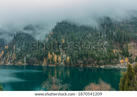 A foggy view of the mountains covered by snow at turquoise water at long sea during winter season, the largest lake in Jiuzhai Valley, Sichuan, China
