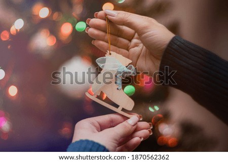Woman holding christmas tree wooden toy in her hands and hanging it on the Christmas fir tree. Winter holidays lights and garlands. Festive mood concept.