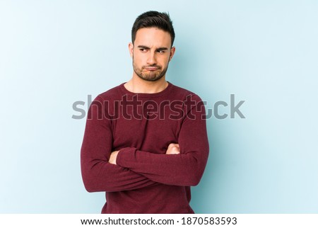 Young caucasian man isolated on blue background frowning face in displeasure, keeps arms folded. Royalty-Free Stock Photo #1870583593