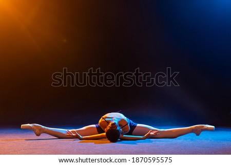 ballerina in a black dress lies in a twine on a black background illuminated by multicolored beams of spotlights