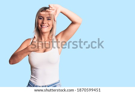 Young beautiful blonde woman wearing casual sleeveless t-shirt smiling making frame with hands and fingers with happy face. creativity and photography concept. 