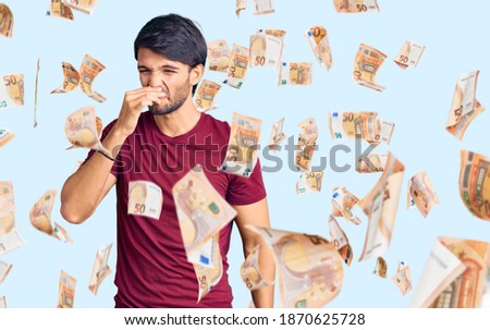 Handsome hispanic man wearing casual clothes smelling something stinky and disgusting, intolerable smell, holding breath with fingers on nose. bad smell