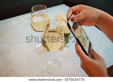 a young woman making picture from two glasses of white wine before drinks, mobile food photo. Concept content for instagram