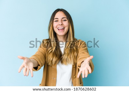 Young caucasian woman isolated on blue background feels confident giving a hug to the camera.