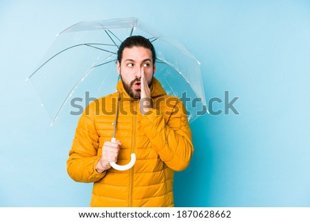 Young man wearing a long hair look holding an umbrella isolated is saying a secret hot braking news and looking aside