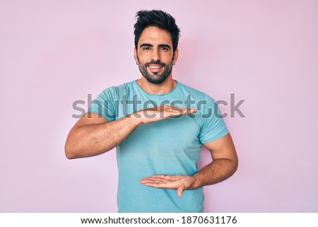 Handsome hispanic man with beard wearing casual clothes gesturing with hands showing big and large size sign, measure symbol. smiling looking at the camera. measuring concept. 