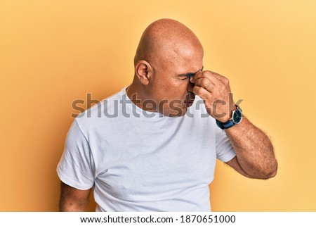 Mature middle east man wearing casual white tshirt tired rubbing nose and eyes feeling fatigue and headache. stress and frustration concept. 