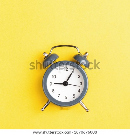 Gray alarm clock on the yellow background. Minimal styled photo.