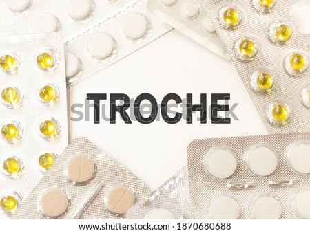 Text troche on white background. There are various pills and vitamins around. Medicine concept