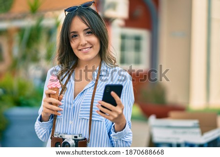 Young hispanic tourist woman using smartphone and eating ice cream at the city.