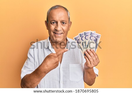 Handsome mature man holding 5000 japanese yen banknotes smiling happy pointing with hand and finger 