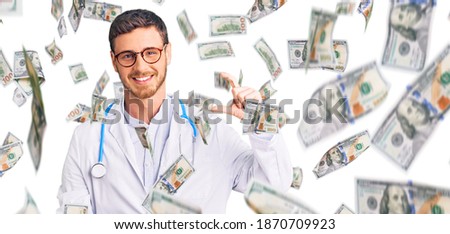 Handsome young man with bear wearing doctor uniform smiling and confident gesturing with hand doing small size sign with fingers looking and the camera. measure concept.
