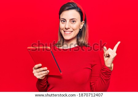 Young beautiful woman holding touchpad smiling happy pointing with hand and finger to the side 