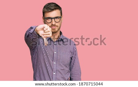 Handsome caucasian man wearing casual clothes and glasses looking unhappy and angry showing rejection and negative with thumbs down gesture. bad expression. 
