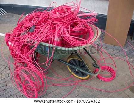 Wheelbarow filled with rolls pink optical fiber cables. Construction site. High speed or 5G internet, part of a serie.