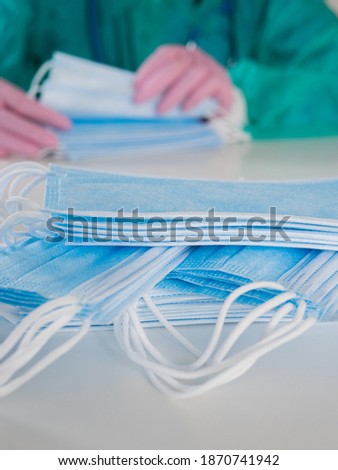 A doctor wearing disposable blue gloves takes a stack of medical masks from a light table and counts their number.