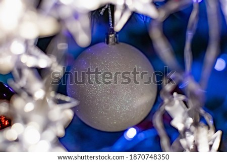 Interesting Christmas toys on the Christmas tree. Christmas accessories in white, among flashing lanterns and lights. Festive and elegant cute things for family holidays.