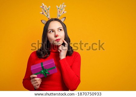 happy young woman with christmas deer antlers with gift on yellow background isolated