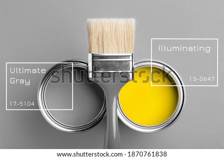 Two cans of yellow and gray paint with gray brush on gray background with inscriptions. Top view, repair concept.