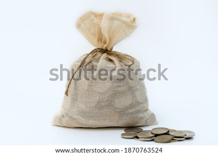 a closed and tied bag with money, several coins nearby. Concept - saving money, protecting cash, gift, inheritance, treasure. Horizontal photo isolated on a white background. Royalty-Free Stock Photo #1870763524