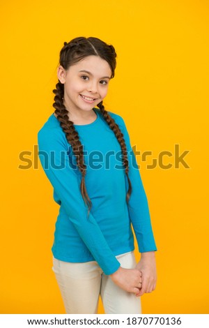 she is shy. happy teen girl with stylish hairstyle. hairdresser for kid. hair beauty and care. childhood happiness. smiling child on orange background. casual fashion trend. braided hair in pigtails.