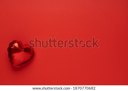 Red balloon in the shape of heart on red background top view flat lay copy space