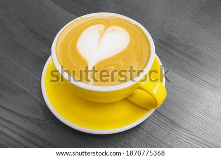 Yellow cup of coffee with heart shaped latte art