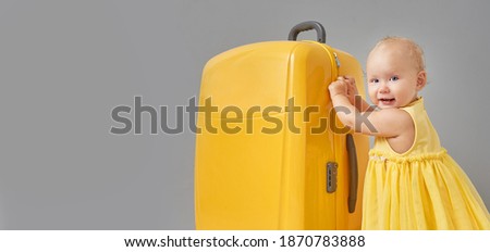 Banner in the trending colors of the year 2021. The concept of travel. A little girl in a yellow dress with a yellow suitcase of Illuminating color and an Ultimate Gray background. Copy space.