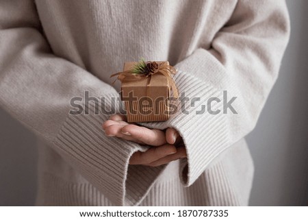 Woman in cozy knitted sweater holding christmas craft gift box. Giving presents concept.