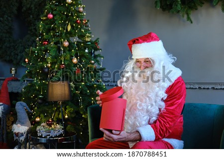 Portret Santa Claus opens magic glowing gift box and looks inside, bright light shines from box.