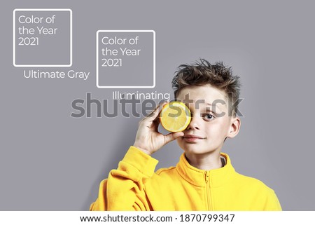 a boy in a bright yellow jacket with a lemon in his hand on a gray background, color of the year 2021