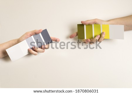 Women's hands hold swatches of the trendy colors - illuminating yellow and ultimate grey. Selection of year 2021 colors for design of clothes, interiors, websites and publications. Flat lay. 