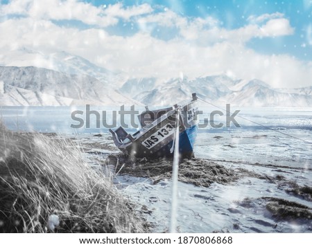 frozen lake and old fishing boat on the background of mountains. it's snowing