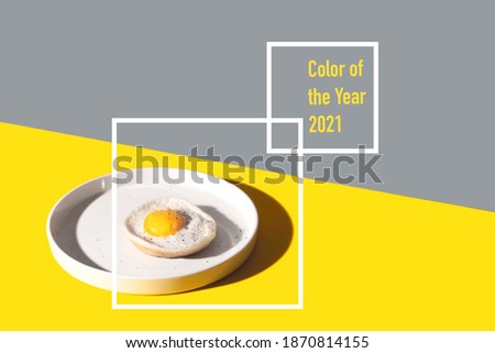 The color of the year 2021 is illuminating yellow and the ultimate gray. Fried egg on a round plate on a yellow table with hard shadows. 