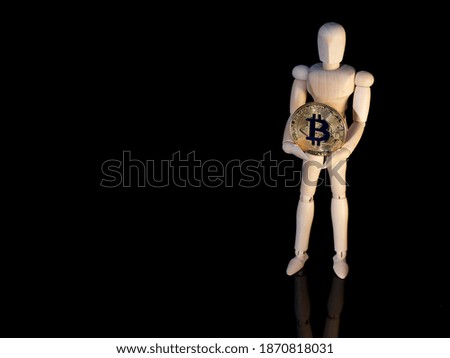 Conceptual photo of cryptocurrency. A small wooden man holds in his hands a round bitcoin coin in golden color.