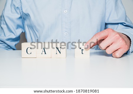 There are wooden cubes with the word CAN't on the table, a man wearing a shirt pushes the cube with the letter t away. The concept of success in business, you can do something.