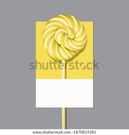 Swirly Illuminating yellow lollipop candy on Ultimate Gray palette card. Color year 2021. Flat lay, minimal.