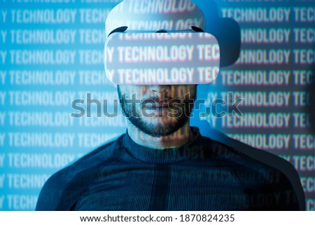 Young man in futuristic costume on blue neon light digital interface background. Guy using VR helmet. Augmented reality, virtual reality, future technology, game concept.