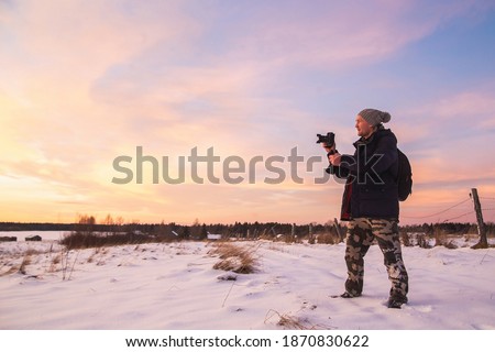 Male amateur photographer takes pictures of colorful winter sunset. Winter fairy tale with purple colors