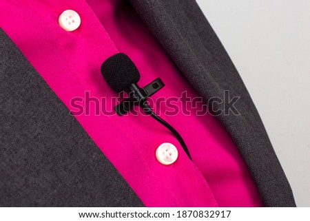 The lavalier microphone is secured with a clip on a women's shirt close-up. Audio recording of the sound of the voice on a condenser microphone