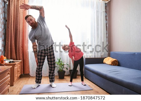 Family doing yoga. Pretty blonde daughter and handsome bearded father doing side tilts as a part of their morning exercise, while spending time at home