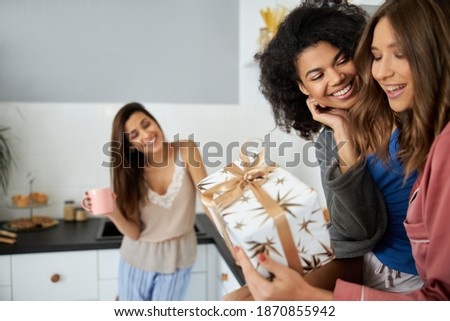 Curly girl giving gift for her best friend. Happy girl gladly accepting it. Stock photo