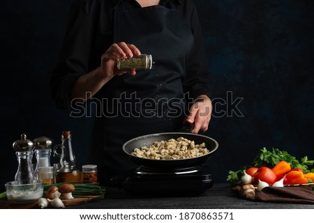 Chef pours hot spices into pan with frying chicken fillet for preparing meat filling for pie. Ingredients for cooking on the background. Dark blue background space. Frozen motion. Cooking process.