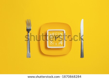 Clock on a plate with cutlery on a yellow background. Lack of time concept. Minimalistic banner with colors of the year 2021 - Illuminating and Ultimate Gray.