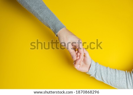 Mom and child in gray clothes holding hands on yellow background. Creative banner with two colors of the year 2021 - Illuminating and Ultimate Gray. Concept of helping children and a strong family.