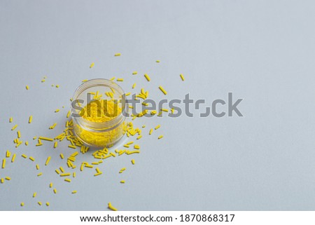 Transparent small jar with yellow pastry sprinkles on a gray background. Minimalistic banner with colors of the year 2021 - Illuminating and Ultimate Gray. Main trend concept with copy space.