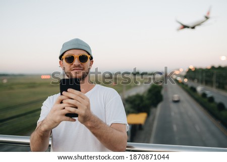 Man in hat and sunglasses standing on the bridge and making selfie. Blurred background