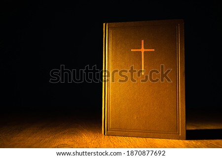 The illuminated Bible stands on a wooden table in the dark. Holy Bible next to the place for text. The Bible is on the pastor's Desk. Catholicism, Protestantism and Orthodoxy. Christian literature.